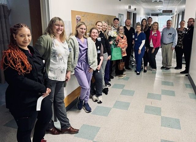 Diverse group of healthcare professionals lined up in a hospital corridor, smiling at the camera.